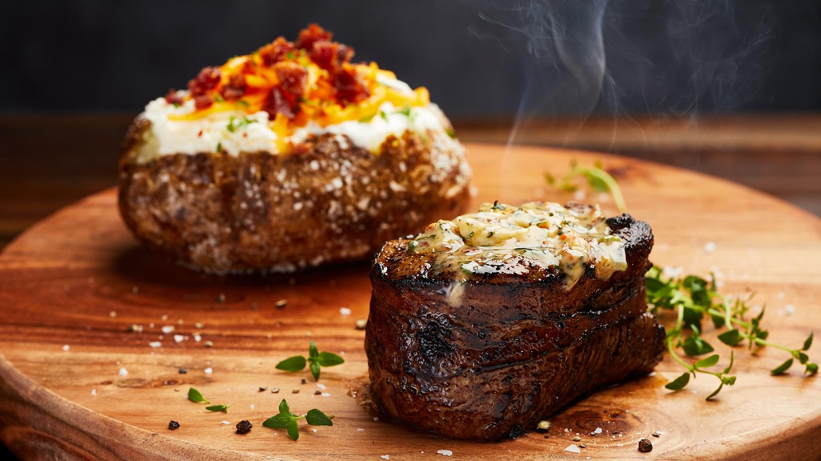 A closeup of a sizzling filet mignon served with a loaded baked potato, a Firebirds dinner favorite.