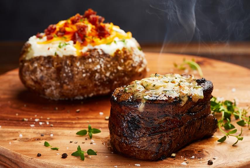 A closeup of a sizzling filet mignon served with a loaded baked potato, a Firebirds dinner favorite.